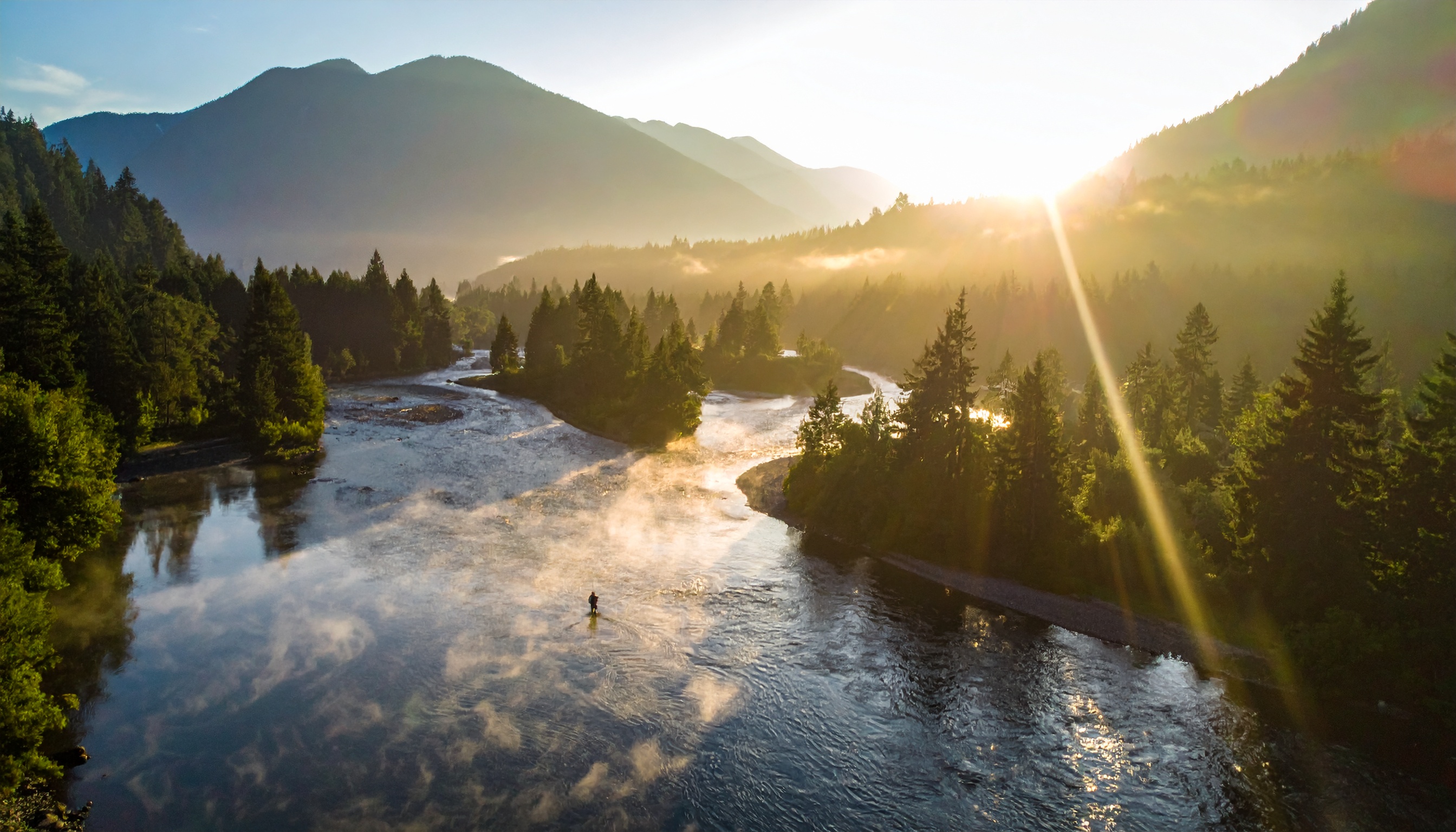 Angler in misty mountain river at golden hour